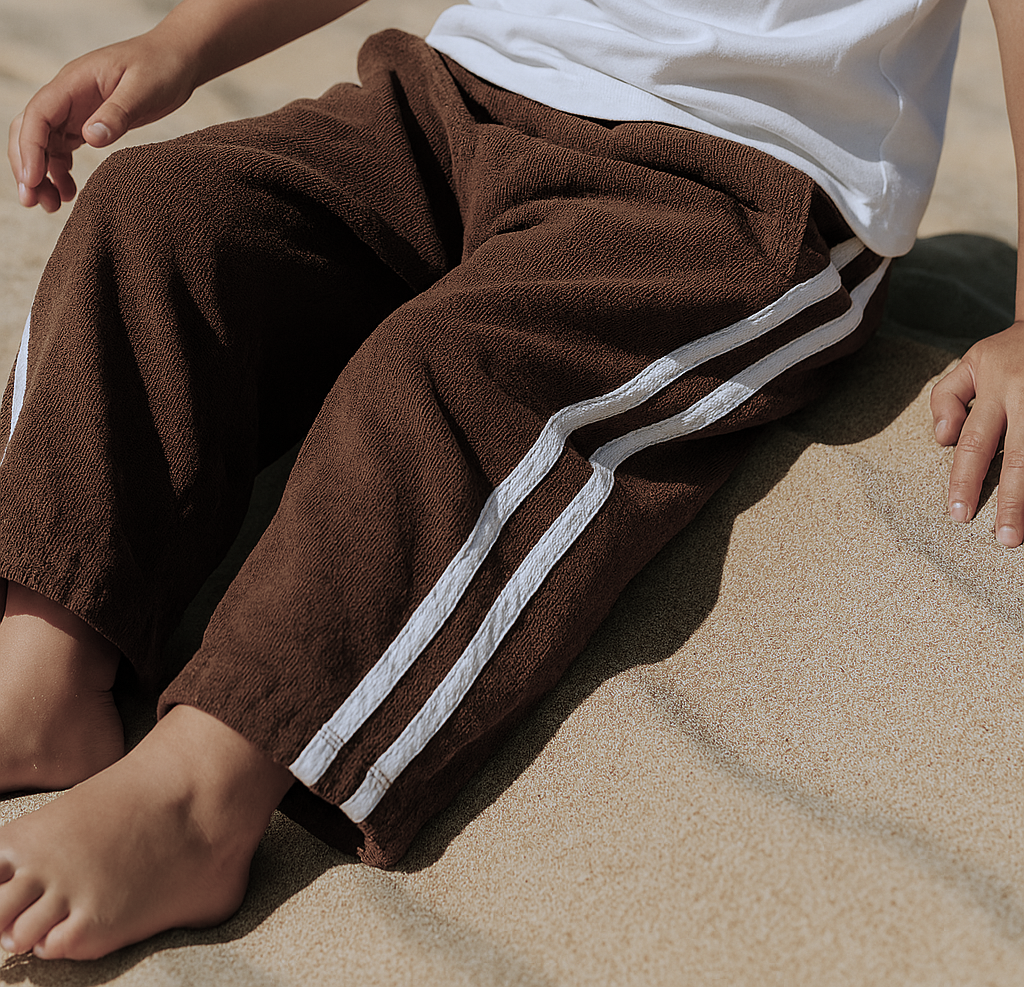 Child wearing brown terry towelling pants with white stripes on a sandy surface