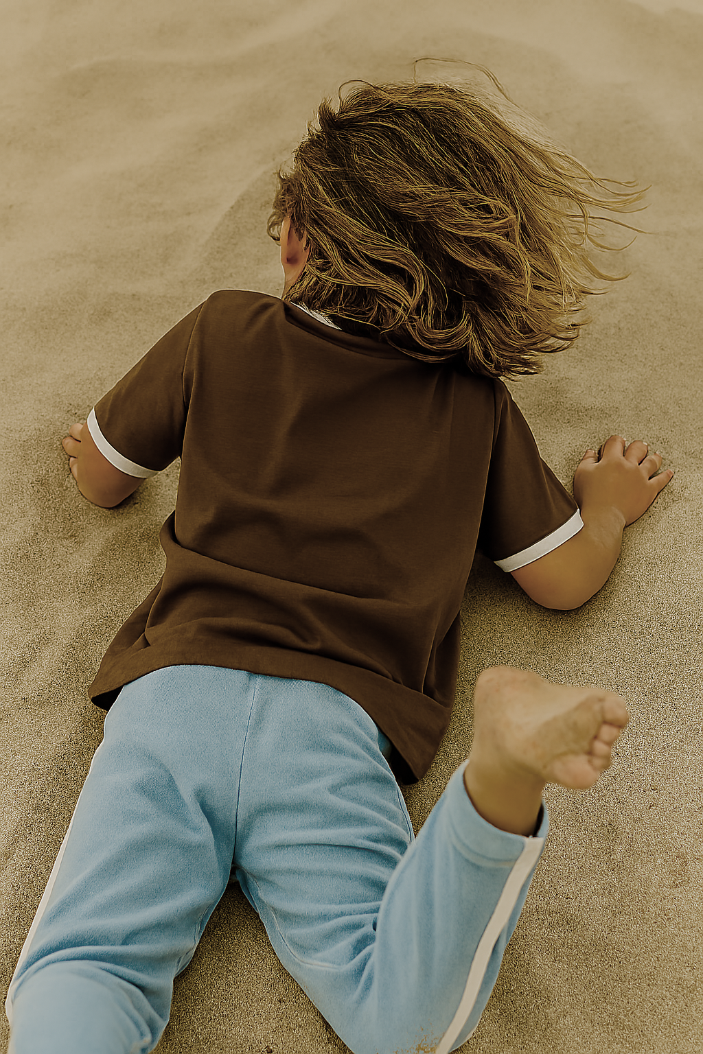 Child at the beach wearing brown shirt with white trims