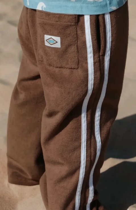 Child wearing brown pants with white stripes and a logo on a blurred background