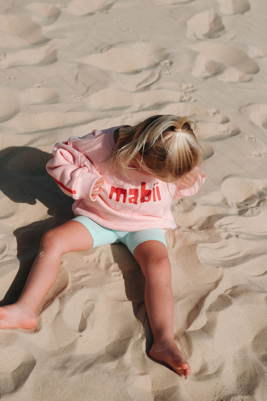 Child wearing a pink jumper with 'mabii' printed on it and two red stripes down the sleeve